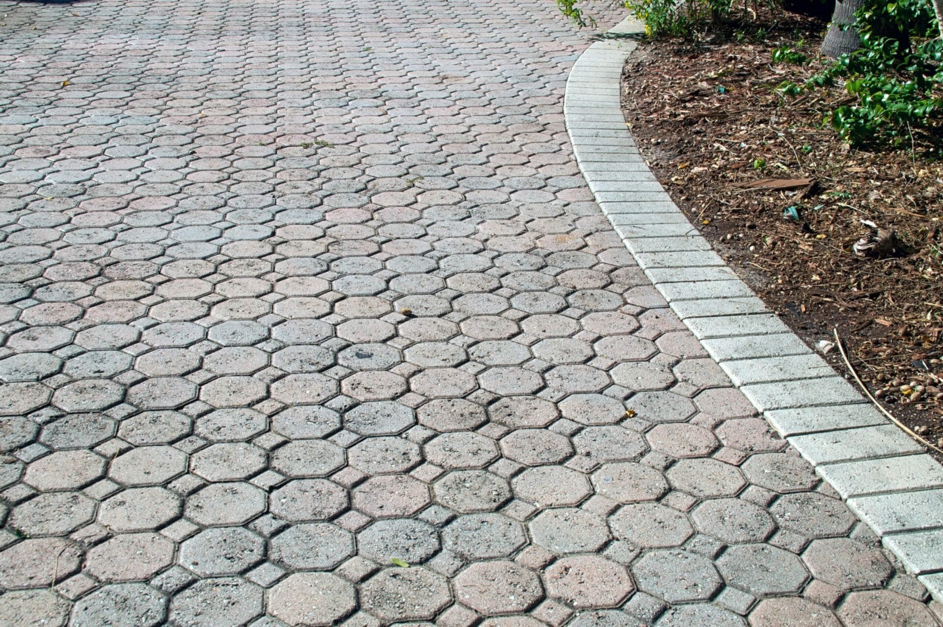 A curved brick pathway with hexagonal pavers in the Bay Area, bordered by a white concrete edge and vegetation on one side.
